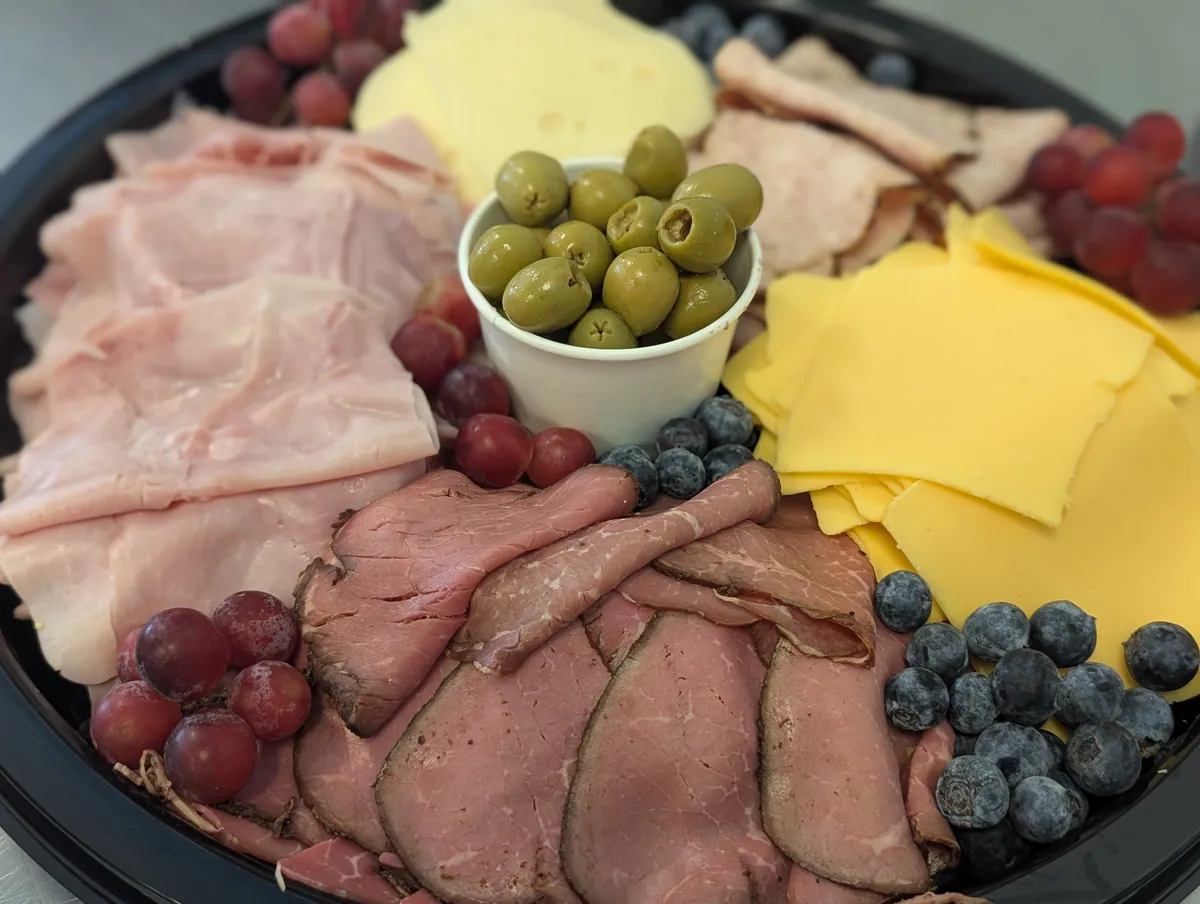 Catering platter with sliced deli meats, cheeses, olives, grapes, and blueberries